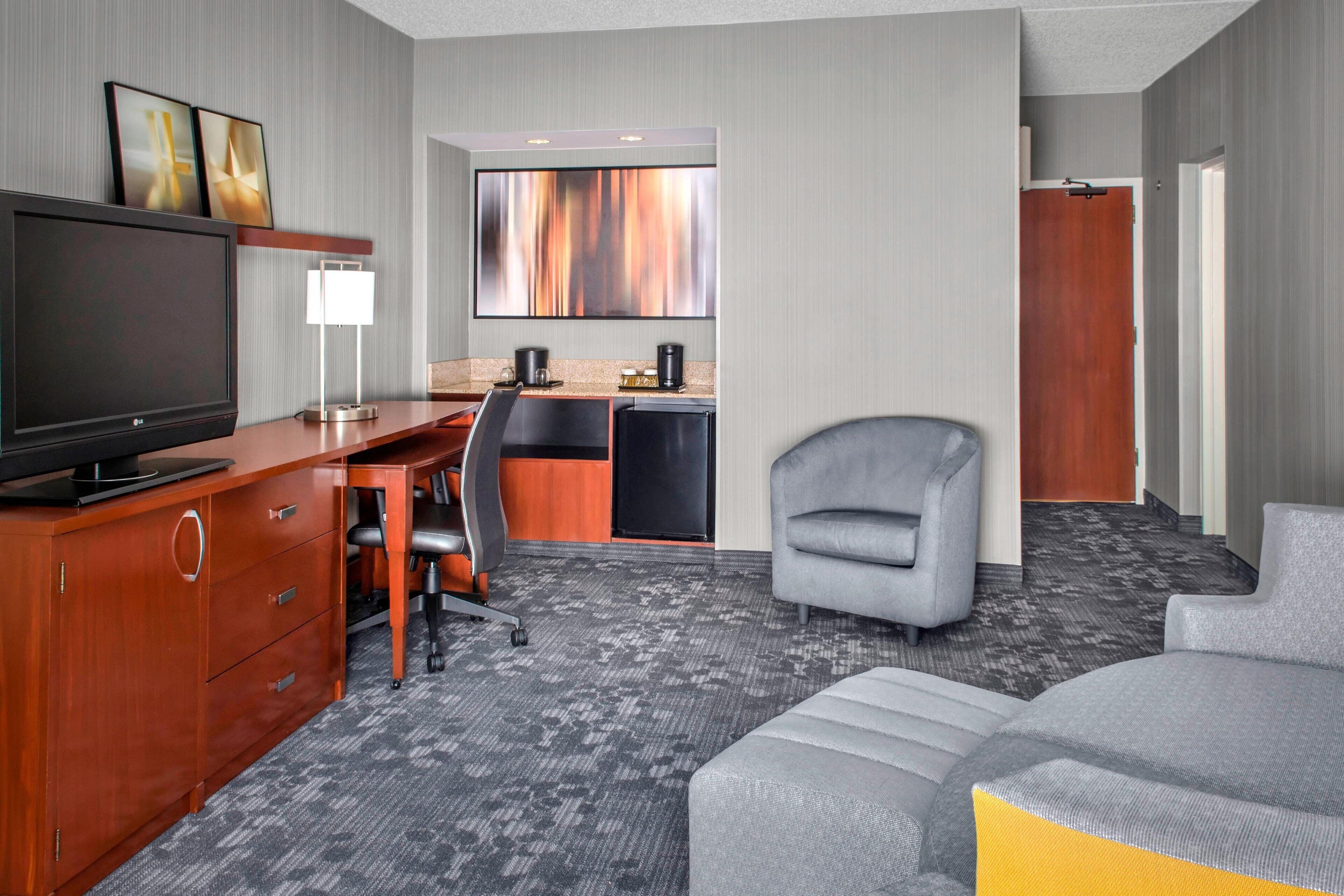 A hotel room with a TV, desk, chair, and sofa.