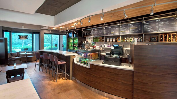 A modern bar area with a wooden counter, bar stools, and a menu board. - Courtyard by Marriott Rye (Rye Brook)