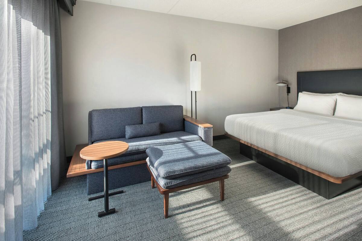A modern hotel room with a bed, a sofa, a small table, and a lamp.