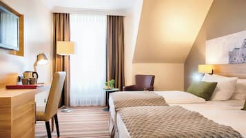 A hotel room with a bed, a desk with a lamp, a chair, a TV, and a window with curtains.