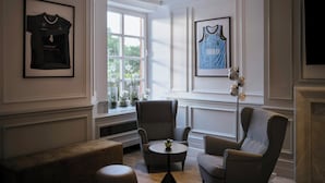 Une pièce avec une cheminée, des maillots de sport encadrés, une fenêtre donnant sur un beau paysage et une table ronde avec une théière.