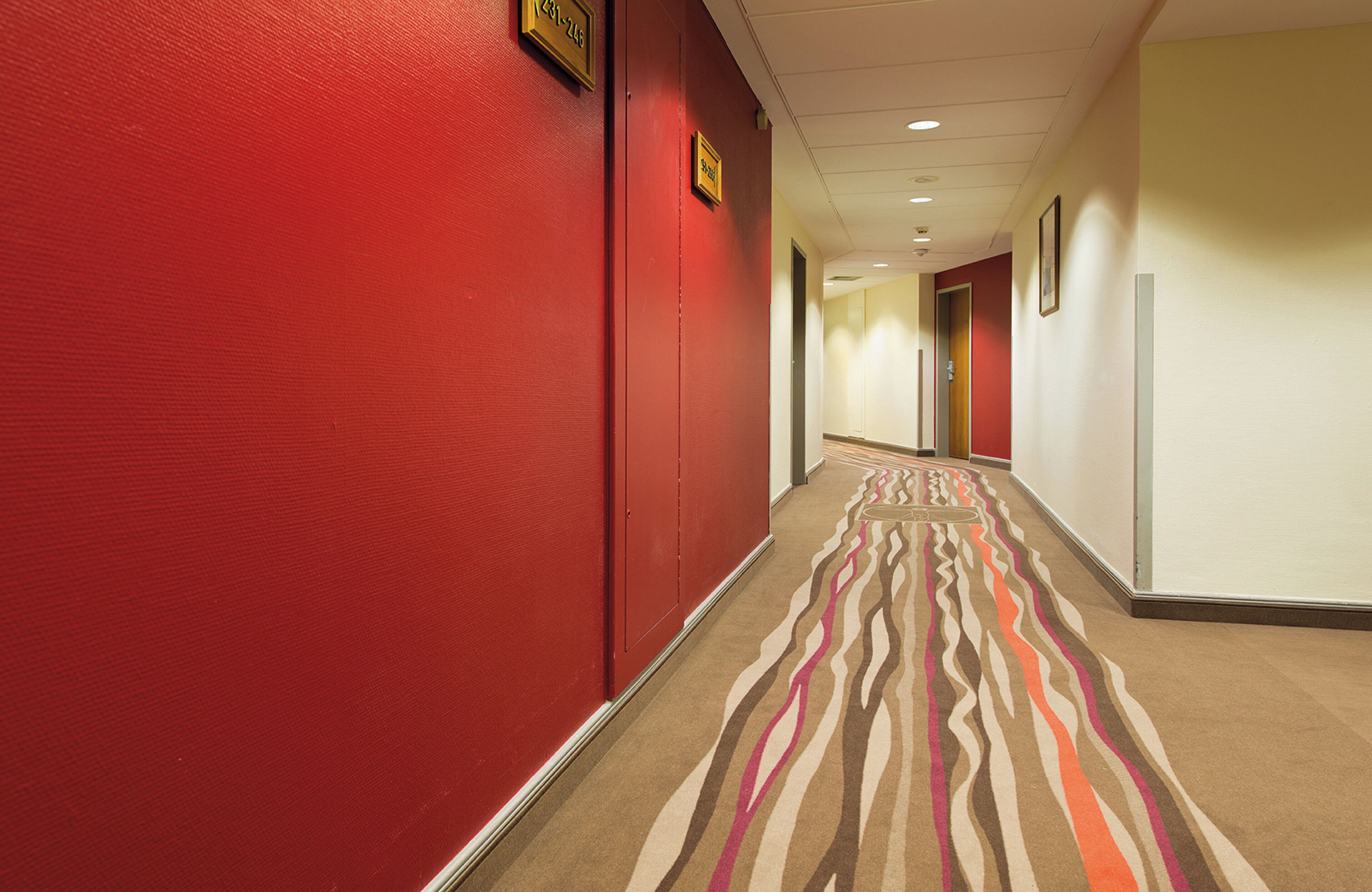 Un corridoio d'albergo con pareti rosse e una moquette fantasia.