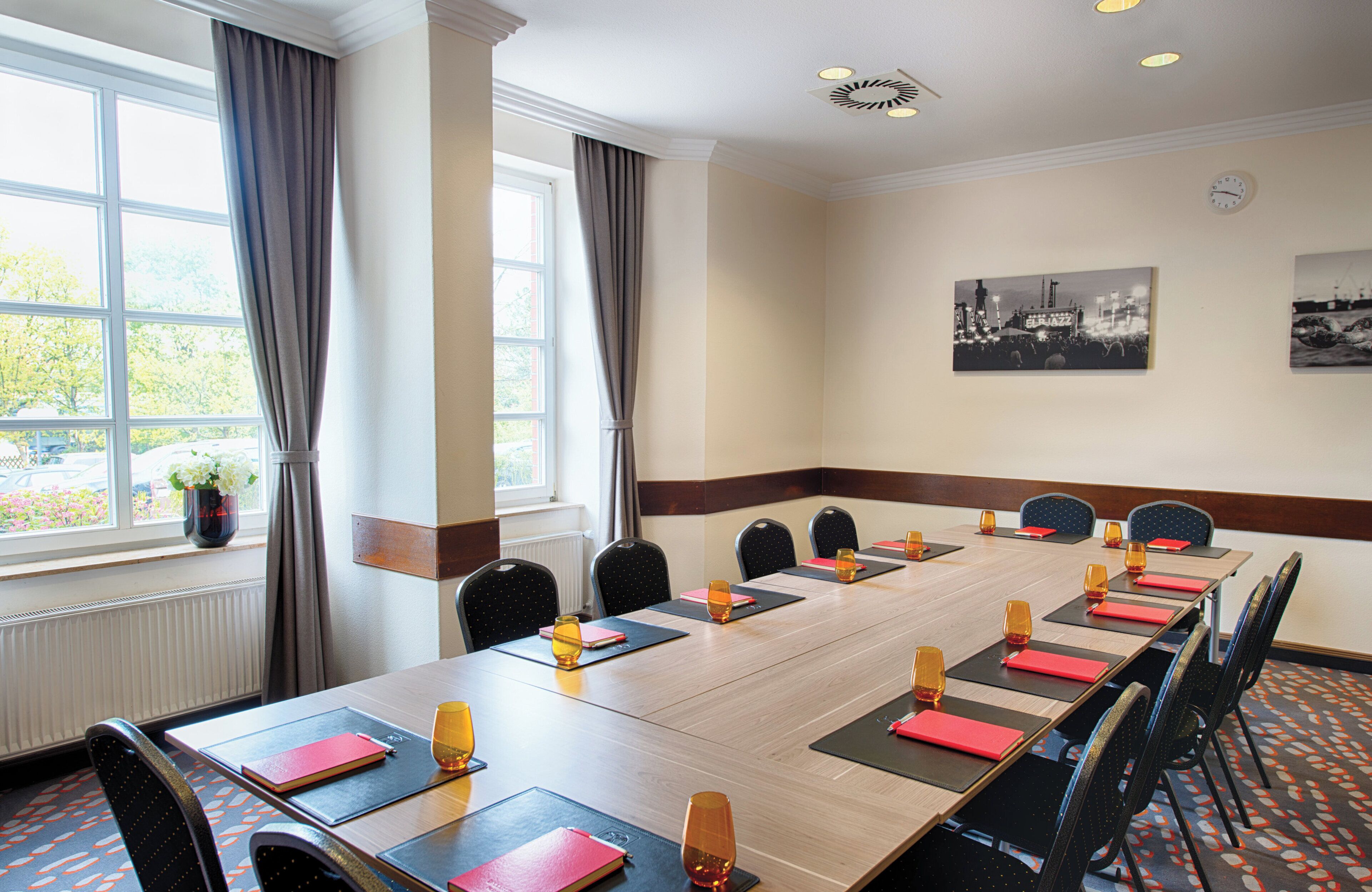 A conference room with a long table, chairs, and a window with curtains.