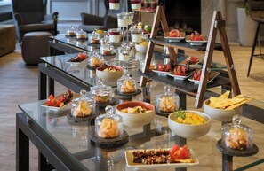 Une table de buffet proposant divers plats et un présentoir à bouteilles dans un hôtel au décor moderne.