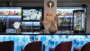 Un coin bar équipé d’un téléviseur diffusant un match de basket-ball, d’une tireuse à bière et d’un vase décoratif rempli de fleurs.