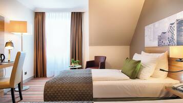 Una habitación de hotel con una cama, un escritorio con lámpara, una silla y una mesita con una planta.