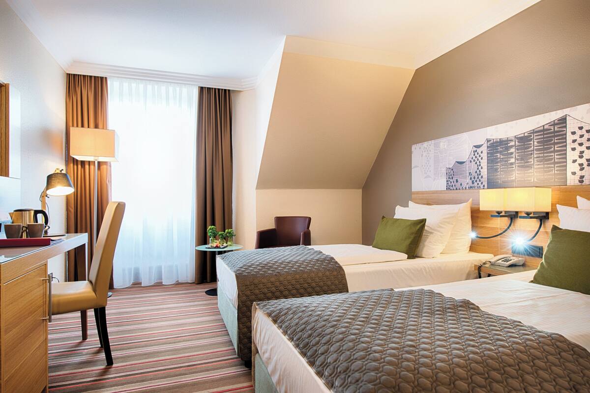Ein Hotelzimmer mit zwei Betten, einem Schreibtisch, einem Stuhl, einer Lampe und einem Bild an der Wand.