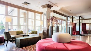 Un hall d’entrée spacieux, doté de grandes fenêtres, d’un pouf rouge et d’un coin salon avec un canapé et des fauteuils.