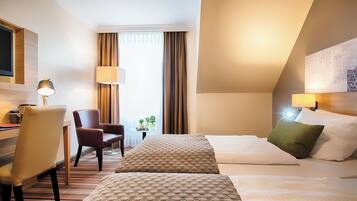 Habitación de hotel con dos camas, un escritorio, una silla, una lámpara y una ventana con cortinas.