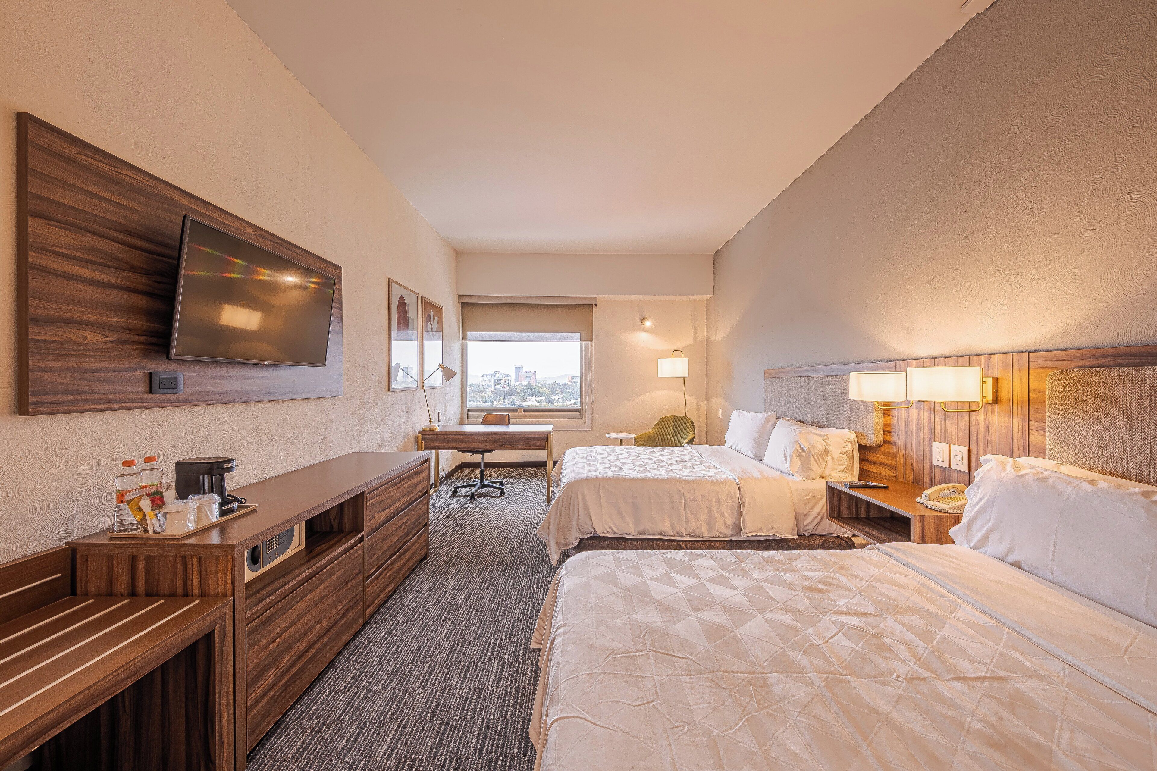 Habitación de hotel con dos camas, un escritorio, un televisor y vistas a la ciudad.