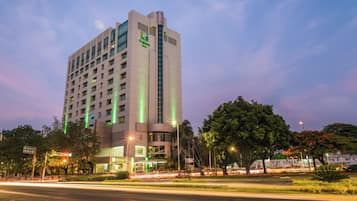 A multi-story hotel with a prominent green logo, a ground-level entrance, and a parking area in front.