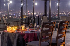 Mesa lista para comer con vista a la ciudad, que incluye mantel, sillas y velas encendidas.