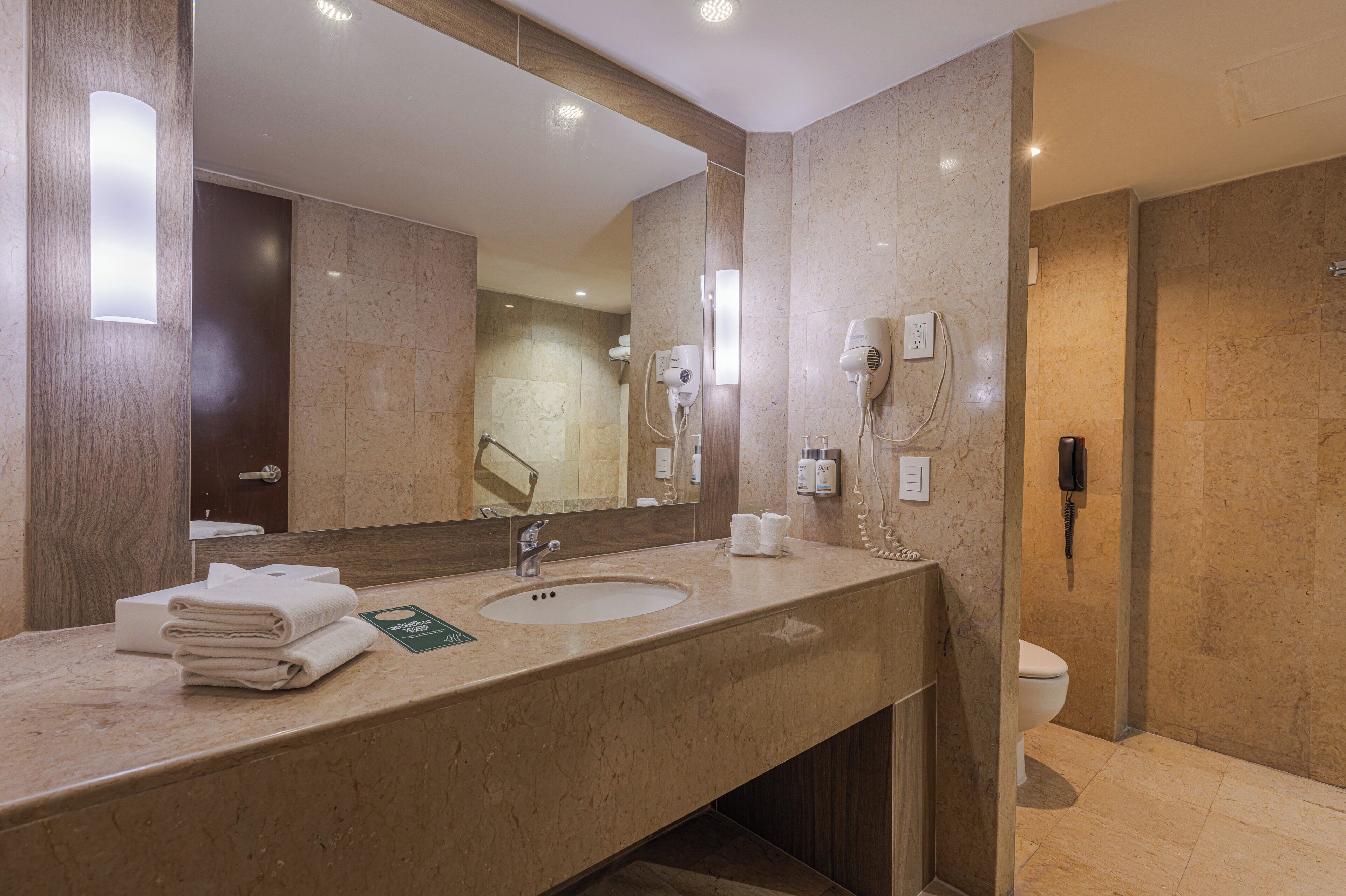 Ein Hotelbad mit einem großen Spiegel, einem Waschbecken, einem Föhn und einem Telefon.