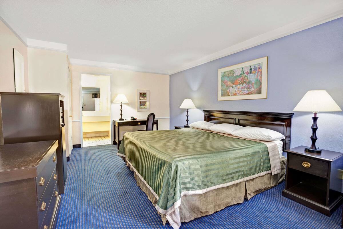 Quarto de hotel com cama, mesas de cabeceira, cômoda e um quadro na parede.