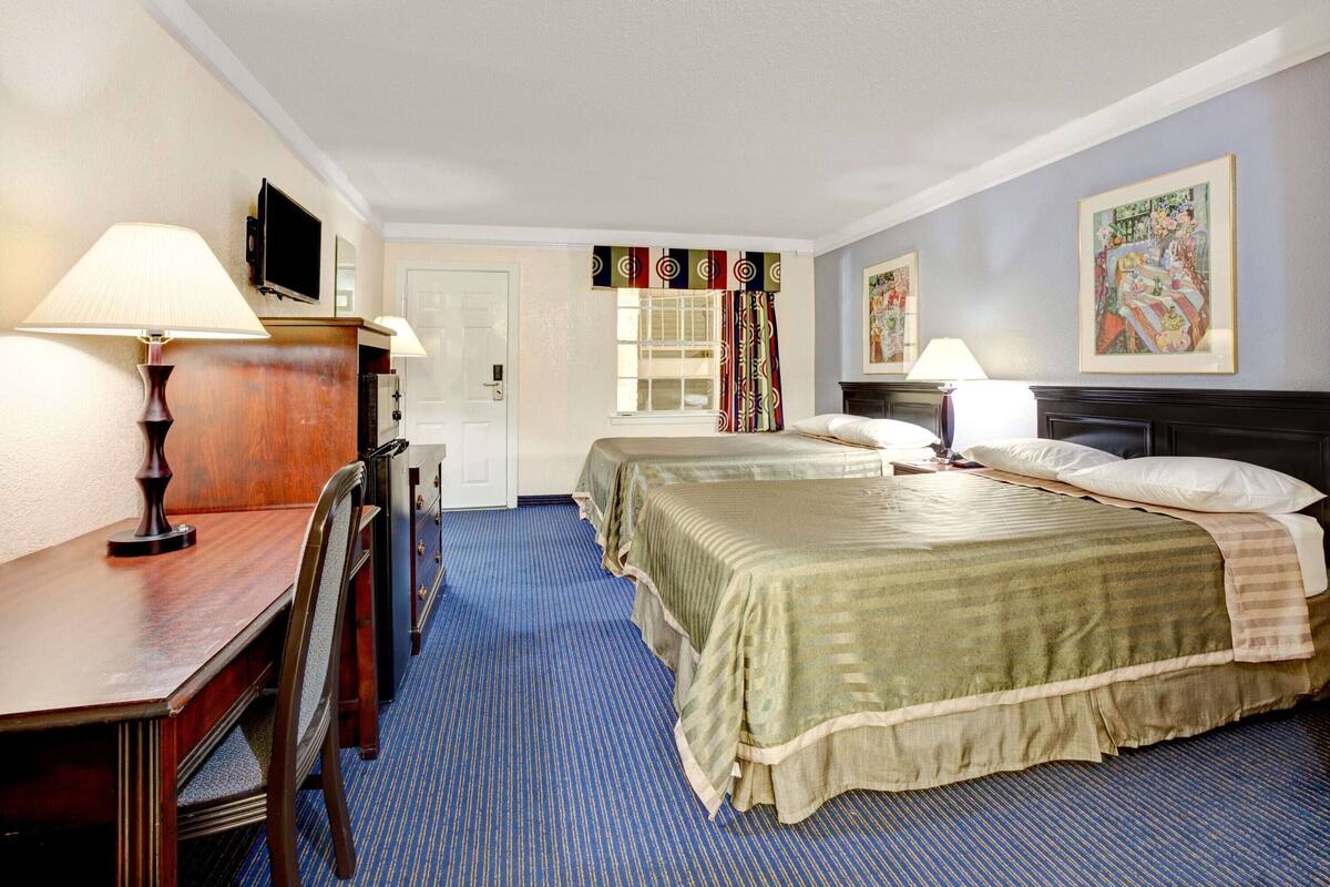 Quarto de hotel com duas camas, uma escrivaninha, televisão e janela com cortinas.