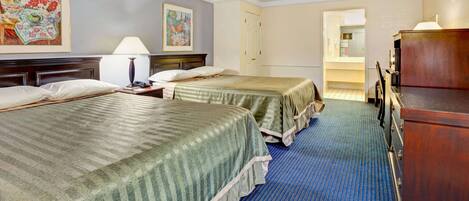 A hotel room with two beds, a dresser, a desk, and a lamp.