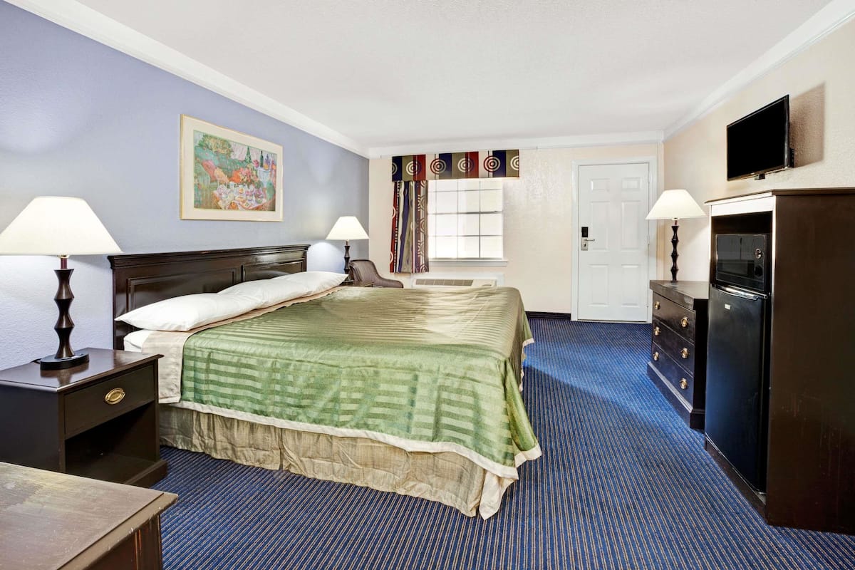 Quarto de hotel com uma cama grande, duas mesas de cabeceira com abajures, uma cômoda, uma televisão e uma janela com cortinas.