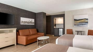Habitación de hotel con sofá, una mesita redonda, cama, televisor, un cuadro y kitchenette.
