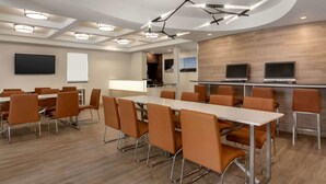 Un salón de conferencias con una larga mesa, sillas anaranjadas, una pizarra y una pantalla de televisión.