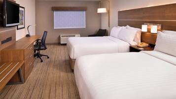 Een hotelkamer met twee bedden, een bureau met stoel, een televisie en een raam met zonwering.