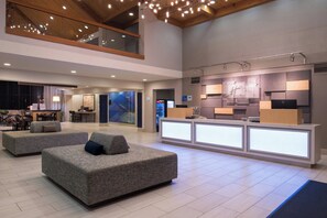 A spacious lobby with a reception desk, seating area, and a high ceiling with exposed beams.
