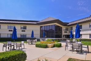 An outdoor patio area with multiple tables and chairs, blue umbrellas, and flower beds. - Holiday Inn Express Walnut Creek by IHG (Walnut Creek)
