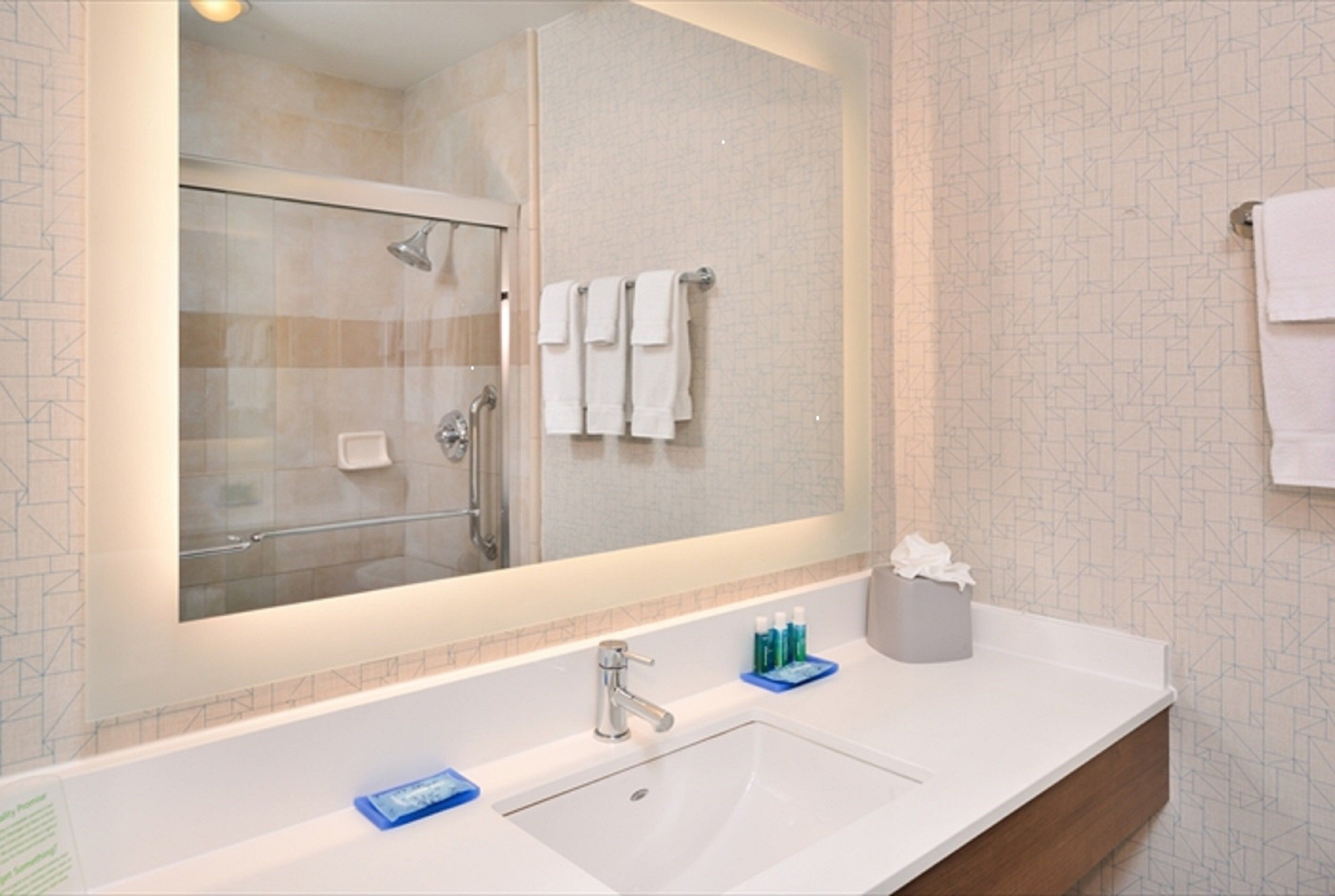 A bathroom with a large mirror, a sink, and a shower.