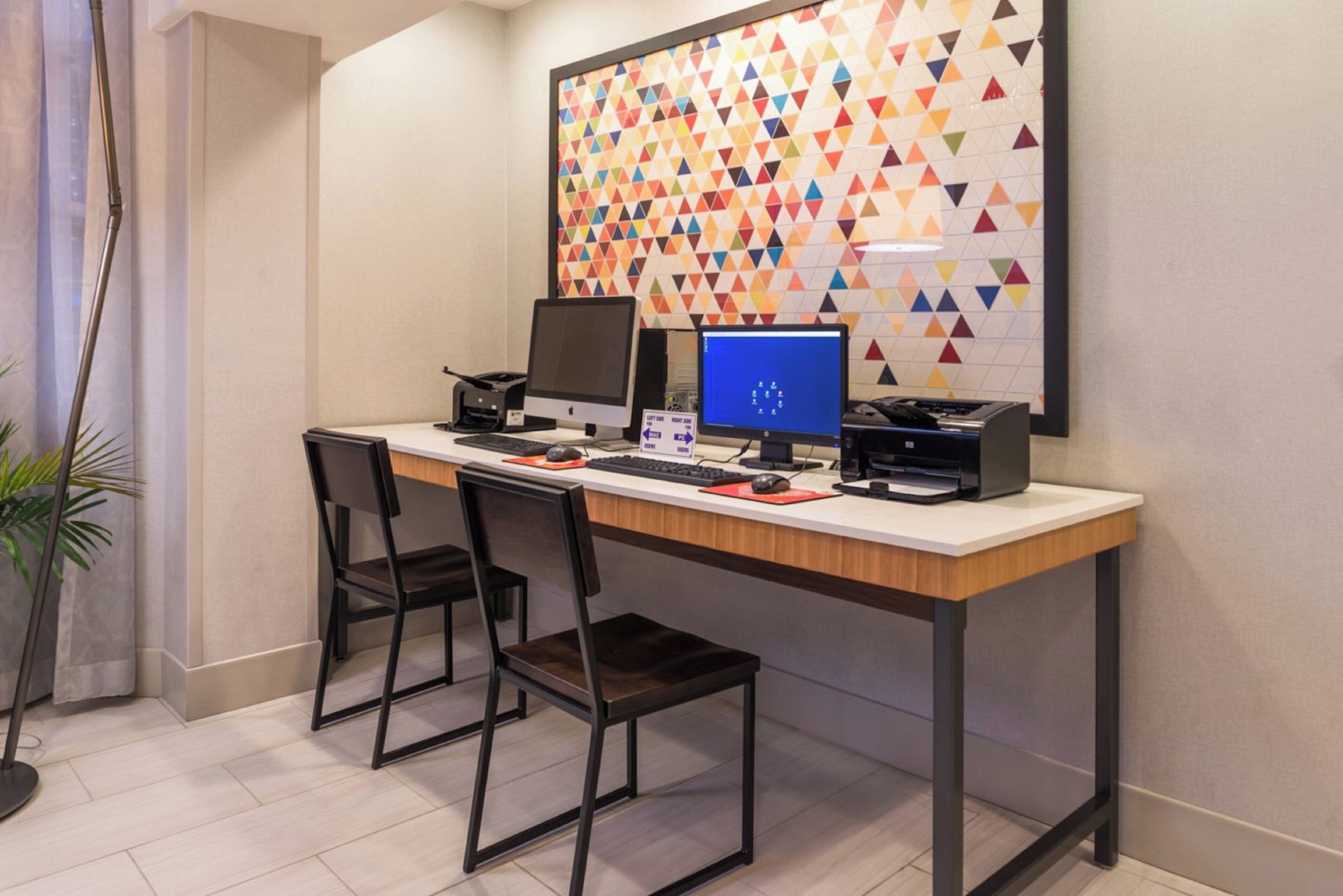 A modern office space with a desk, two chairs, two computers, a printer, and a decorative wall with a geometric pattern.