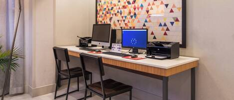 A modern office space with a desk, two chairs, two computers, a printer, and a decorative wall with a geometric pattern.