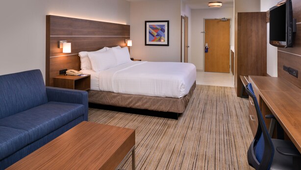 A hotel room with a bed, a blue sofa, a wooden coffee table, a desk with a chair, a TV, and a framed picture on the wall. - Holiday Inn Express Walnut Creek by IHG (Walnut Creek)