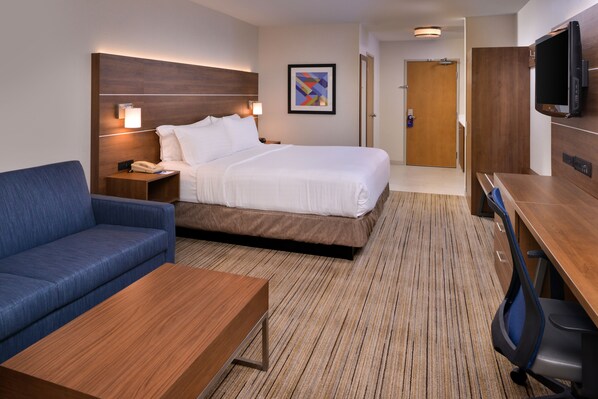 A hotel room with a bed, a blue sofa, a wooden coffee table, a desk with a chair, a TV, and a framed picture on the wall. - Holiday Inn Express Walnut Creek by IHG (Walnut Creek)