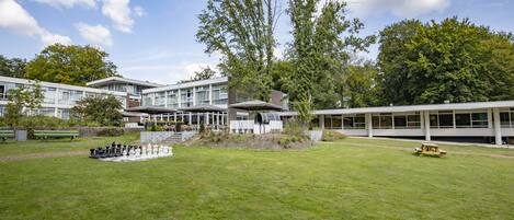 A grassy courtyard with a chessboard, a picnic table, and a building with large windows and a covered area.