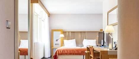 A hotel room with a bed, desk, chair, and a large mirror.