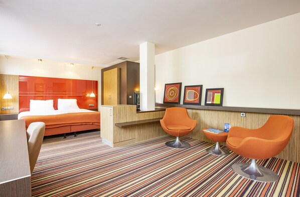 A hotel room with a bed, a desk, two orange chairs, a striped carpet, and framed artwork on the wall. - Fletcher Hotel-Restaurant Amersfoort (Amersfoort)