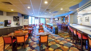 A spacious restaurant with multiple dining tables and chairs, a bar area, and a colorful floor pattern.
