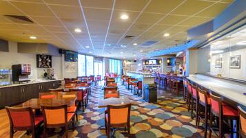 Un restaurante espacioso con varias mesas y sillas, una zona de bar y un colorido diseño en el suelo.