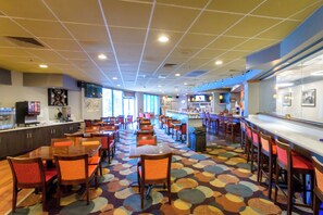 A spacious restaurant with multiple dining tables and chairs, a bar area, and a colorful floor pattern.