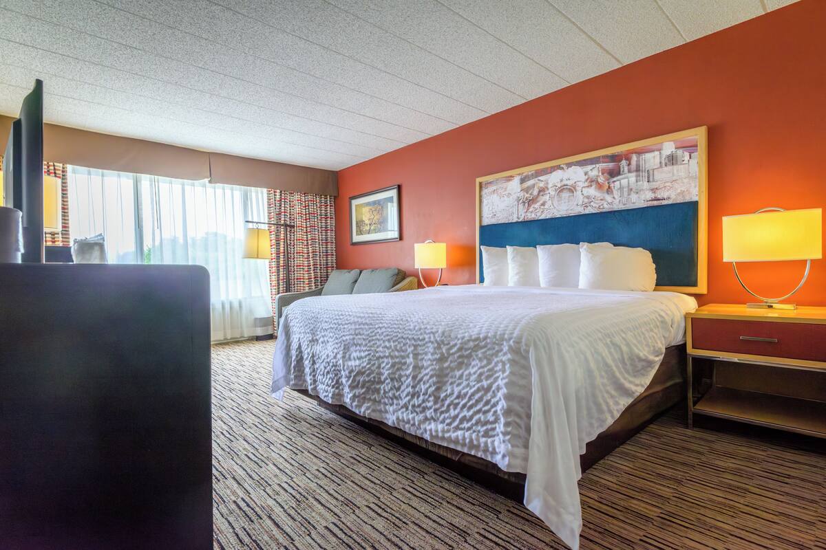 A hotel room with a large bed, a desk, a chair, a lamp, and a window with curtains.