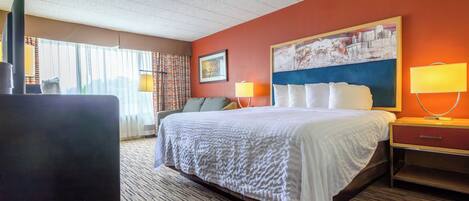 A hotel room with a large bed, a desk, a chair, a lamp, and a window with curtains.