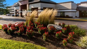 Un bâtiment moderne doté d’un parking et d’un jardin aménagé avec des fleurs rouges.