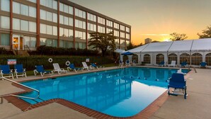 A swimming pool with lounge chairs and umbrellas, a building with large windows, and a sunset in the background.