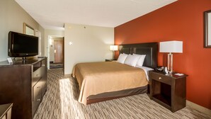 Une chambre d’hôtel avec un lit, un téléviseur posé sur une commode, une table de chevet avec une lampe, et une porte donnant sur une autre pièce.