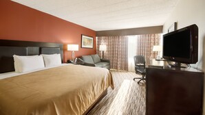 A hotel room with a large bed, a desk with a television, a chair, and a window with curtains.