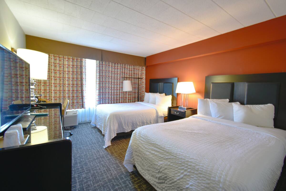 A hotel room with two beds, a desk, a television, and a bathroom.