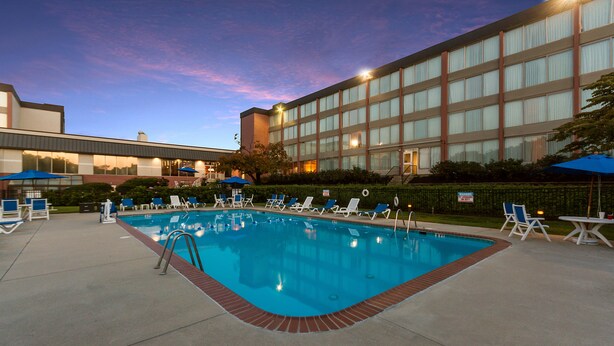 A swimming pool with lounge chairs and umbrellas, surrounded by a building with large windows and a brick border.