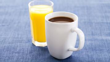 Una taza blanca con café y un vaso de jugo de naranja sobre una superficie de tela azul.
