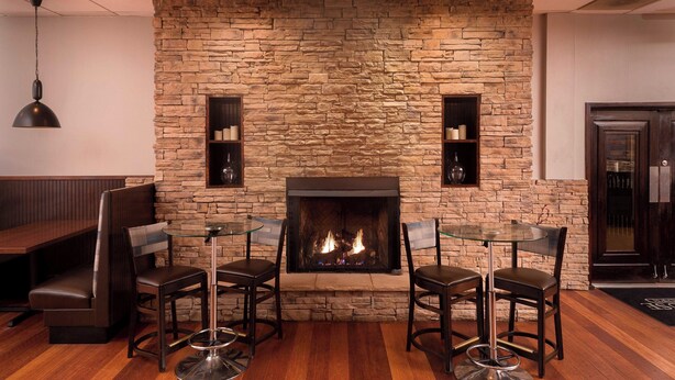 Una habitación acogedora con chimenea de piedra, suelo de madera y una zona de estar con taburetes de bar y un banco.