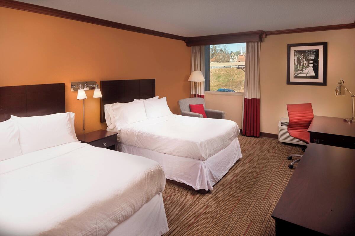 Une chambre d’hôtel avec deux lits, un bureau, une chaise et une fenêtre donnant sur un immeuble.