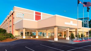 Un hotel con fachada moderna, un cartel llamativo de 'Four Points by Sheraton' y un estacionamiento con espacios delimitados.