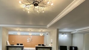 Uma área de recepção de hotel com design moderno, incluindo um balcão de atendimento, um posto de computadores e um candelabro.